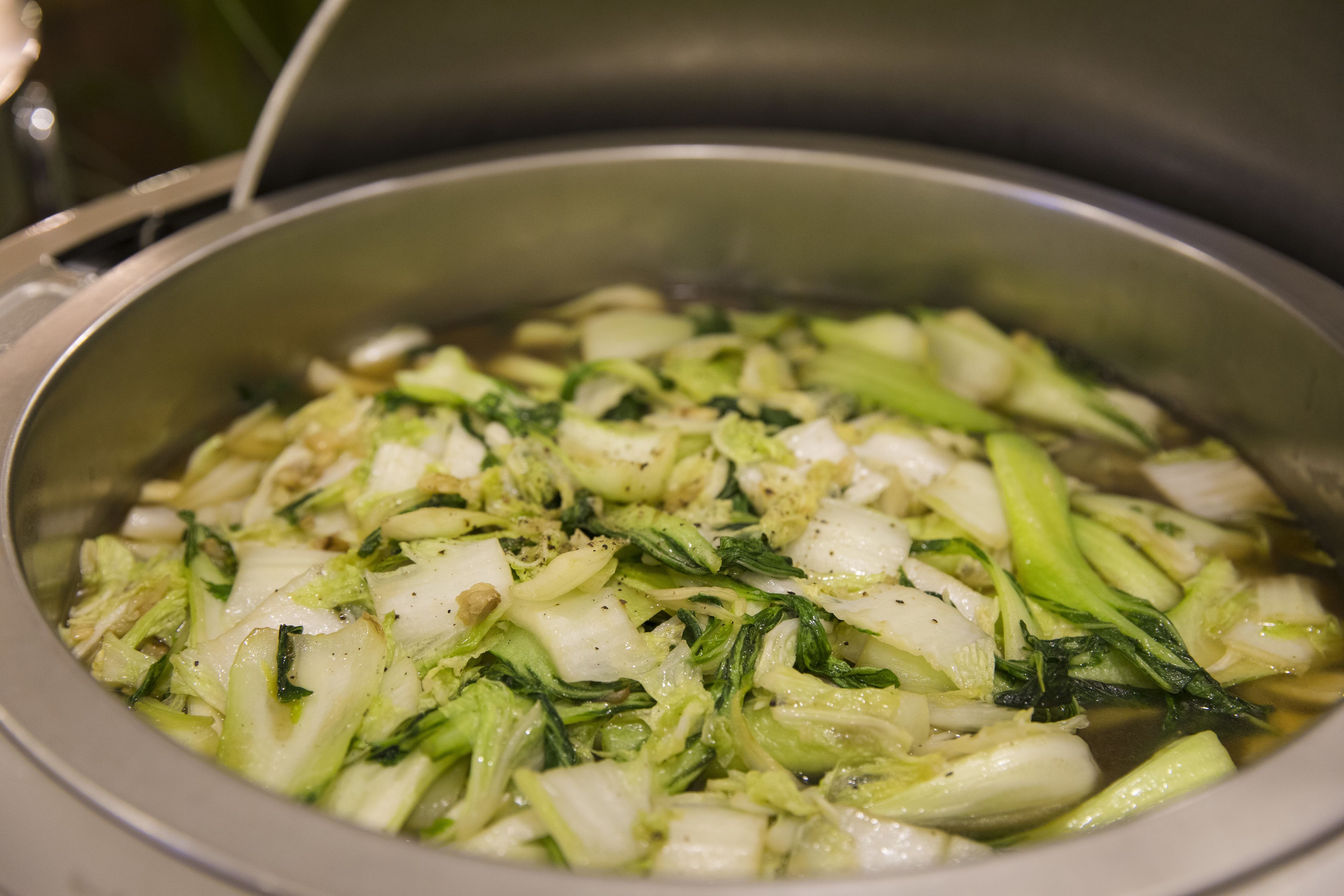 A stainless steel pot containing cooked vegetables, likely cabbage, with visible seasoning.