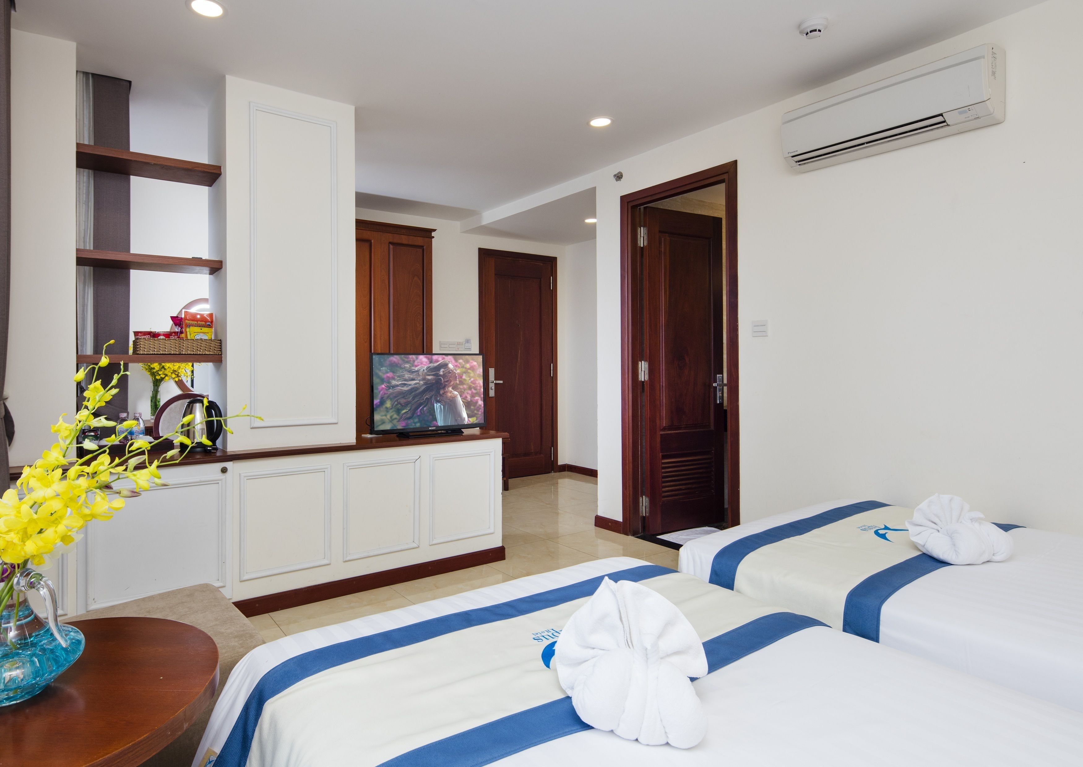 A hotel room with two beds, a television, a mirror, and a bathroom.