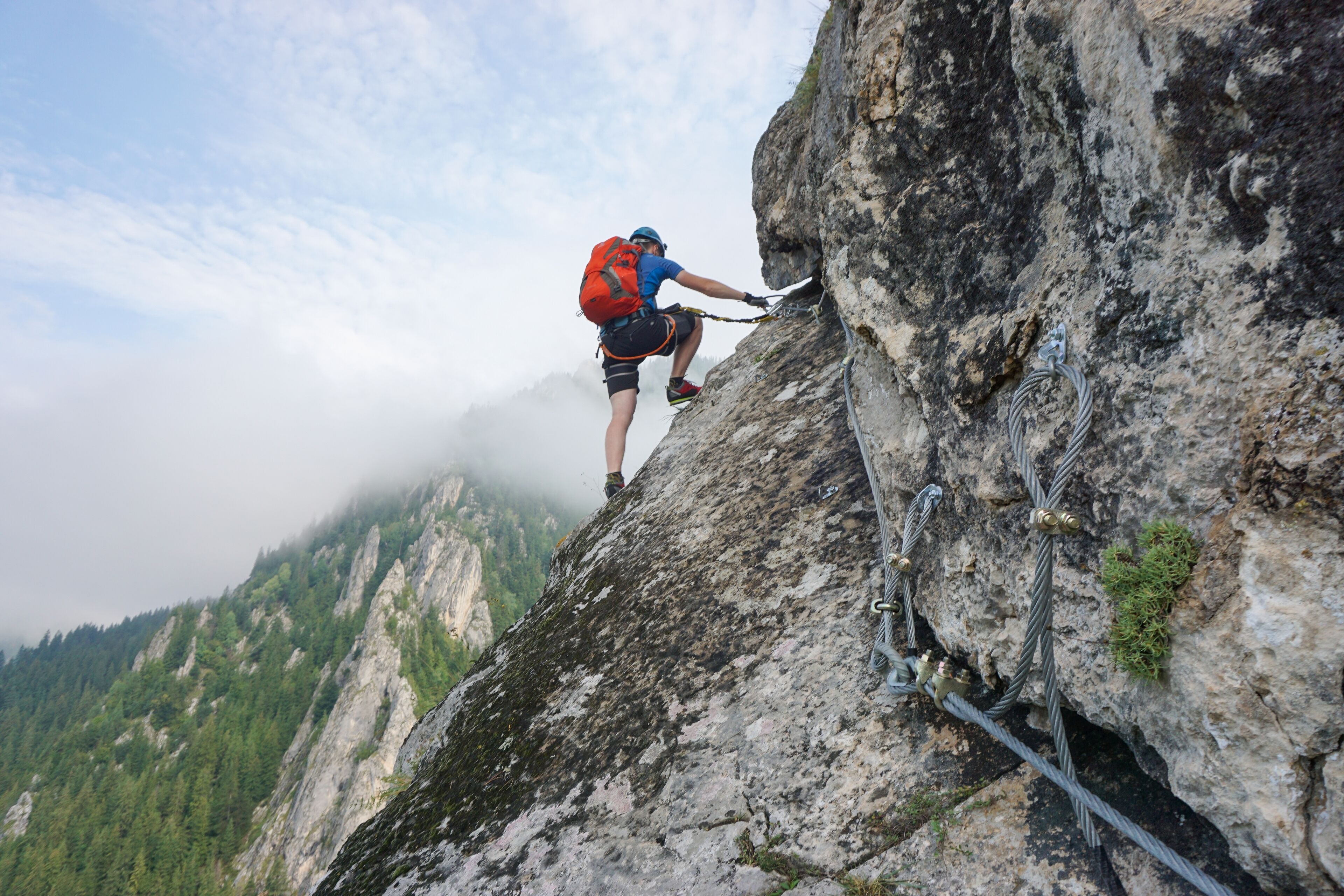 A person climbing a steep rock face with a harness and ropes.