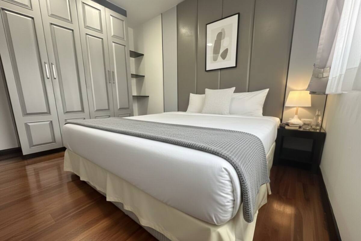 A neatly made bed with a grey blanket, a bedside table with a lamp, and a wardrobe with sliding doors.