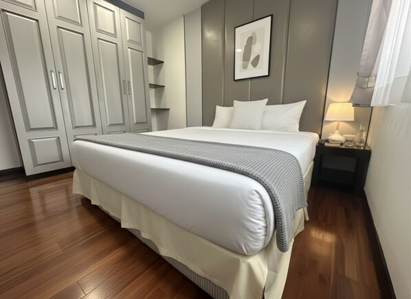 Una cama bien hecha con un edredón gris, una mesita de noche con una lámpara y un armario con puertas correderas.