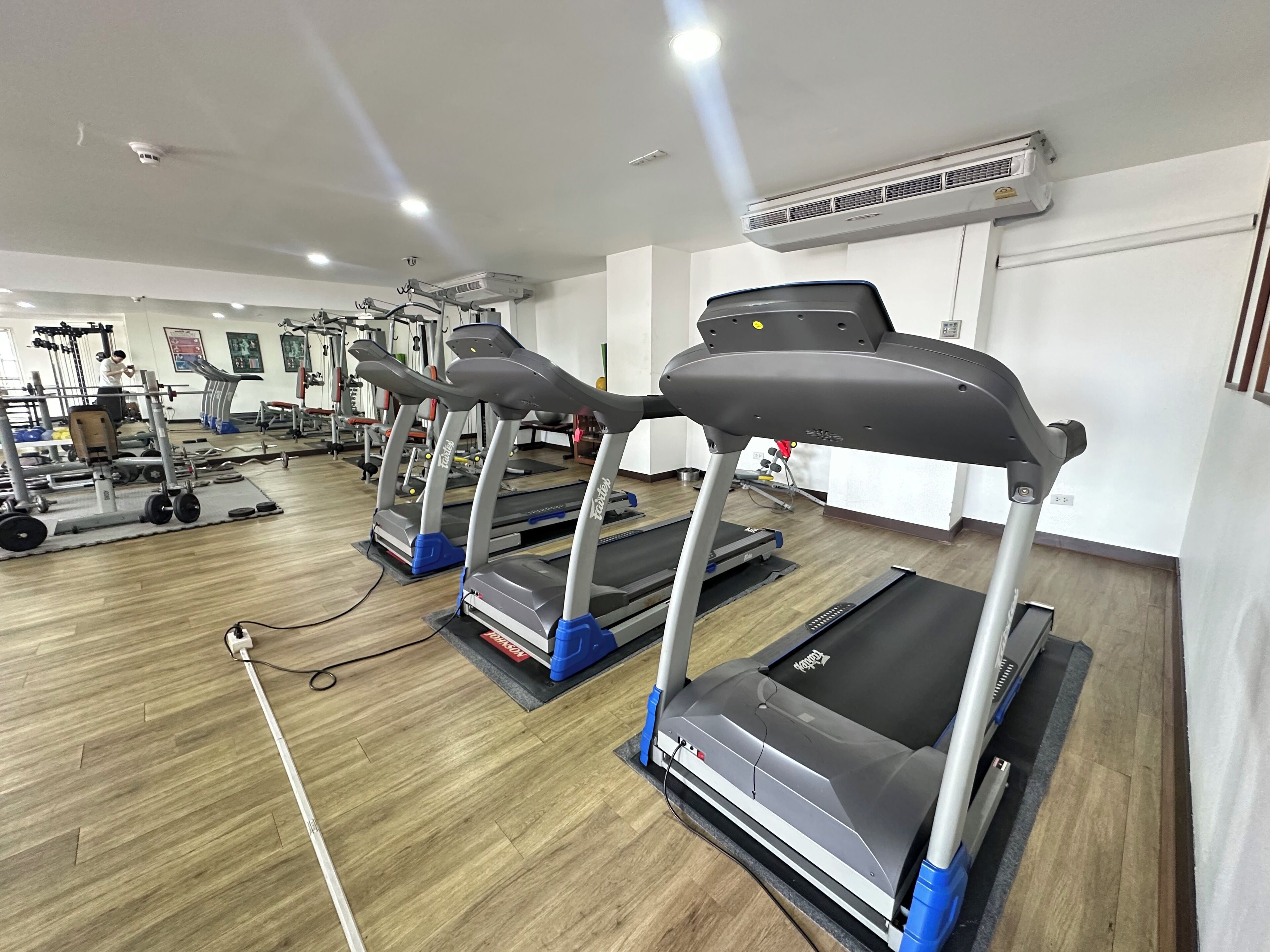 A gym with treadmills, weight machines, and a mirrored wall.