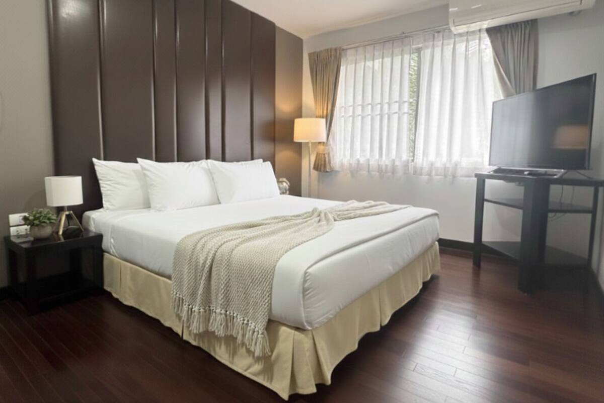 A hotel room with a large bed, a TV, a bedside lamp, and a window with curtains.