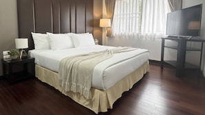 Una habitación de hotel con una cama grande, televisor, lámpara de noche y ventana con cortinas.