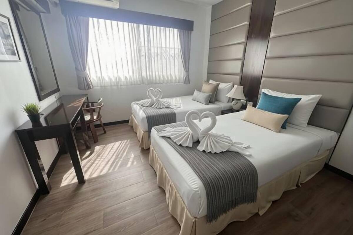 Une chambre d’hôtel avec deux lits, un bureau et une fenêtre avec des rideaux.