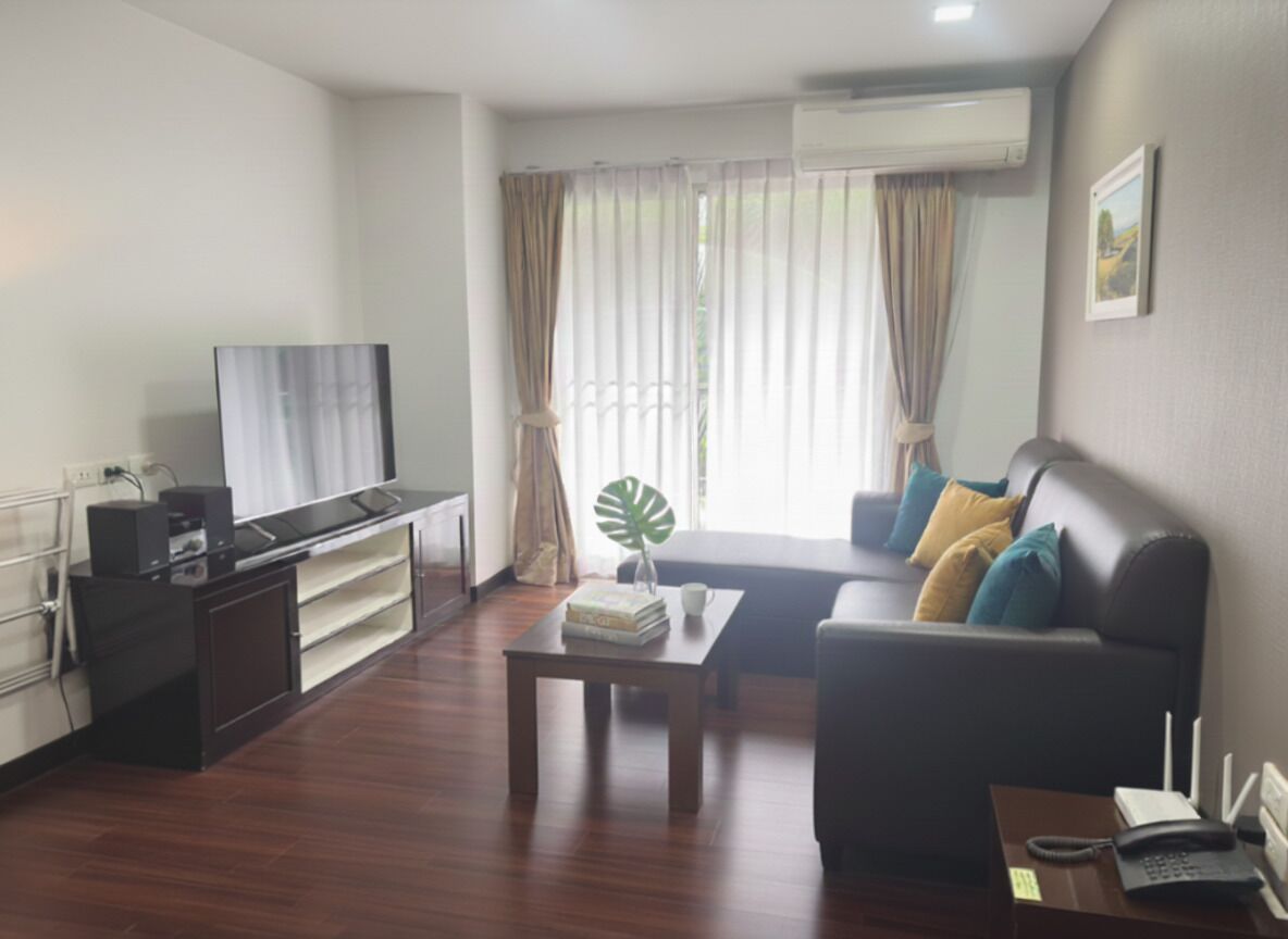 A modern living room with a flat-screen TV, a sofa with cushions, a coffee table, and a small side table with a phone and a book.