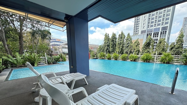 Zona de piscina con sillones de descanso y vista a un edificio identificado como "PACIFIC PARK".