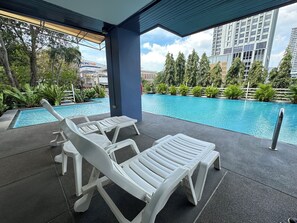 Zona de piscina con sillones de descanso y vista a un edificio identificado como "PACIFIC PARK".
