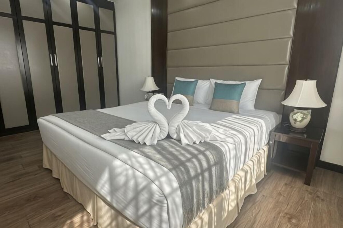 A neatly made bed with a white and gray striped bedspread, two pillows, and a decorative swan-shaped pillow arrangement. There are two bedside lamps on wooden nightstands.