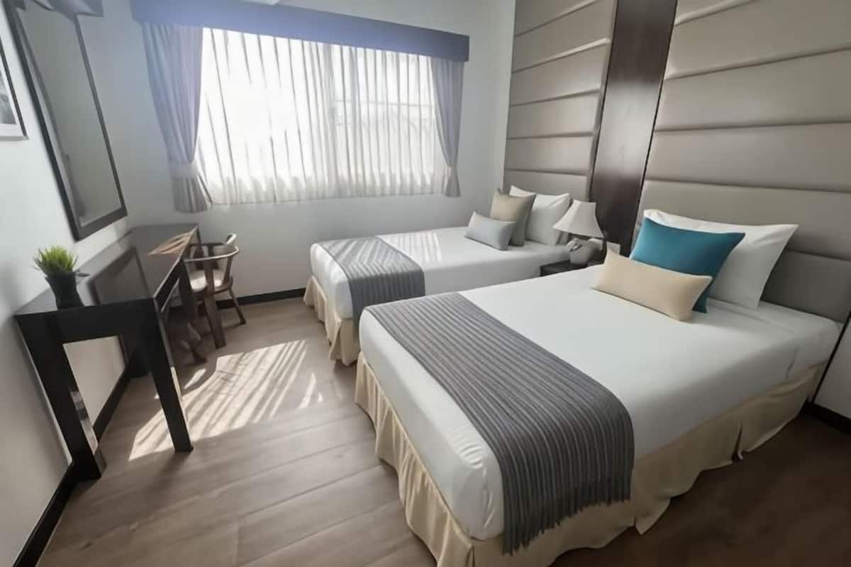 Une chambre dâhĂŽtel avec deux lits, un bureau, une chaise, une fenĂȘtre avec des rideaux et un miroir.