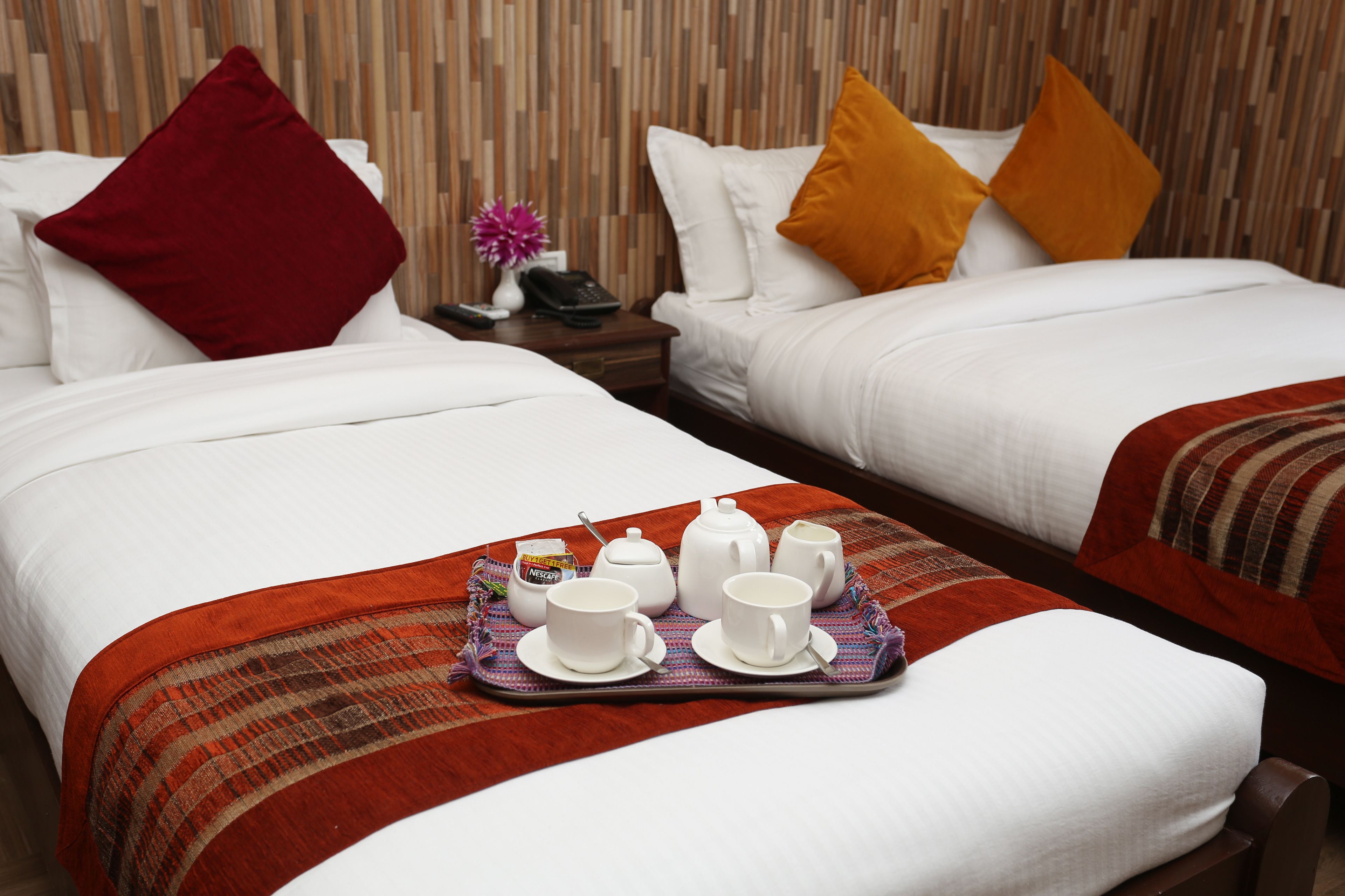 A hotel room with two beds, a tray with tea set, and a nightstand with a vase and phone.