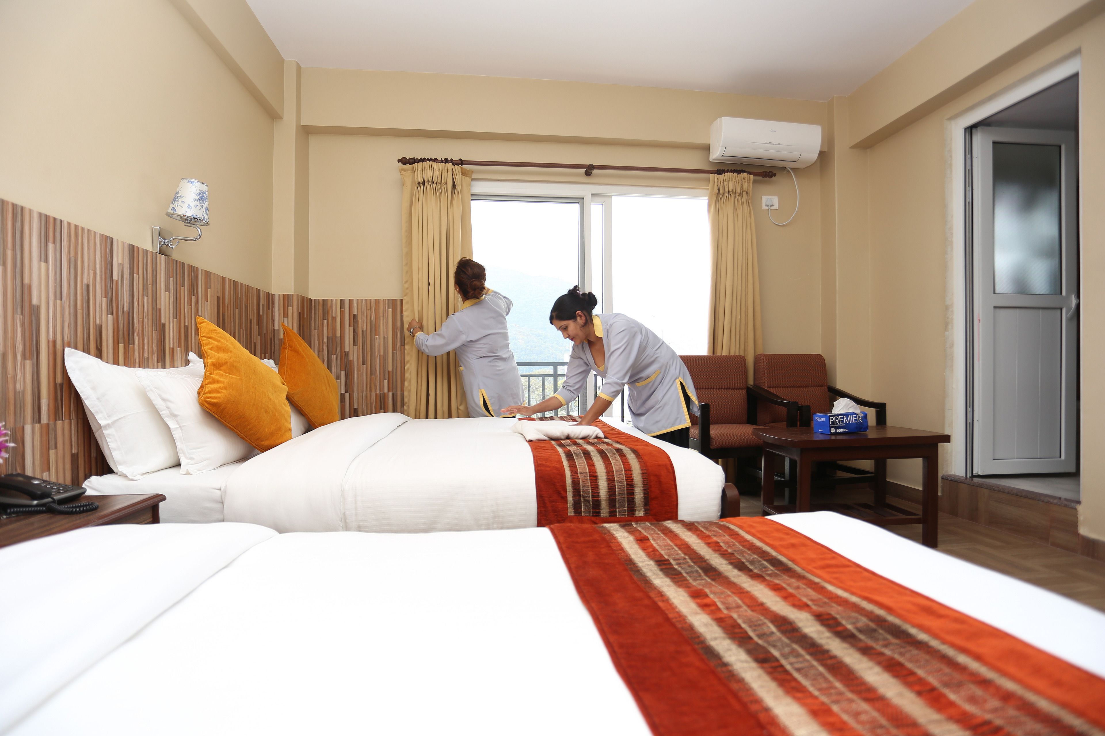 Une chambre d’hôtel avec un grand lit, une tête de lit en bois, un bureau avec une chaise, une fenêtre avec des rideaux et un appareil de climatisation.