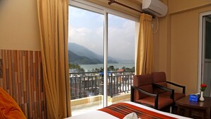 A hotel room with a large bed, a chair, a small table, and a view of a lake and mountains. - Pokhara Choice Inn (Pokhara)