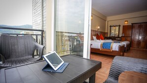 A balcony with wicker furniture and a tablet, a bedroom with a bed and wooden wardrobe, and a city view. - Pokhara Choice Inn (Pokhara)