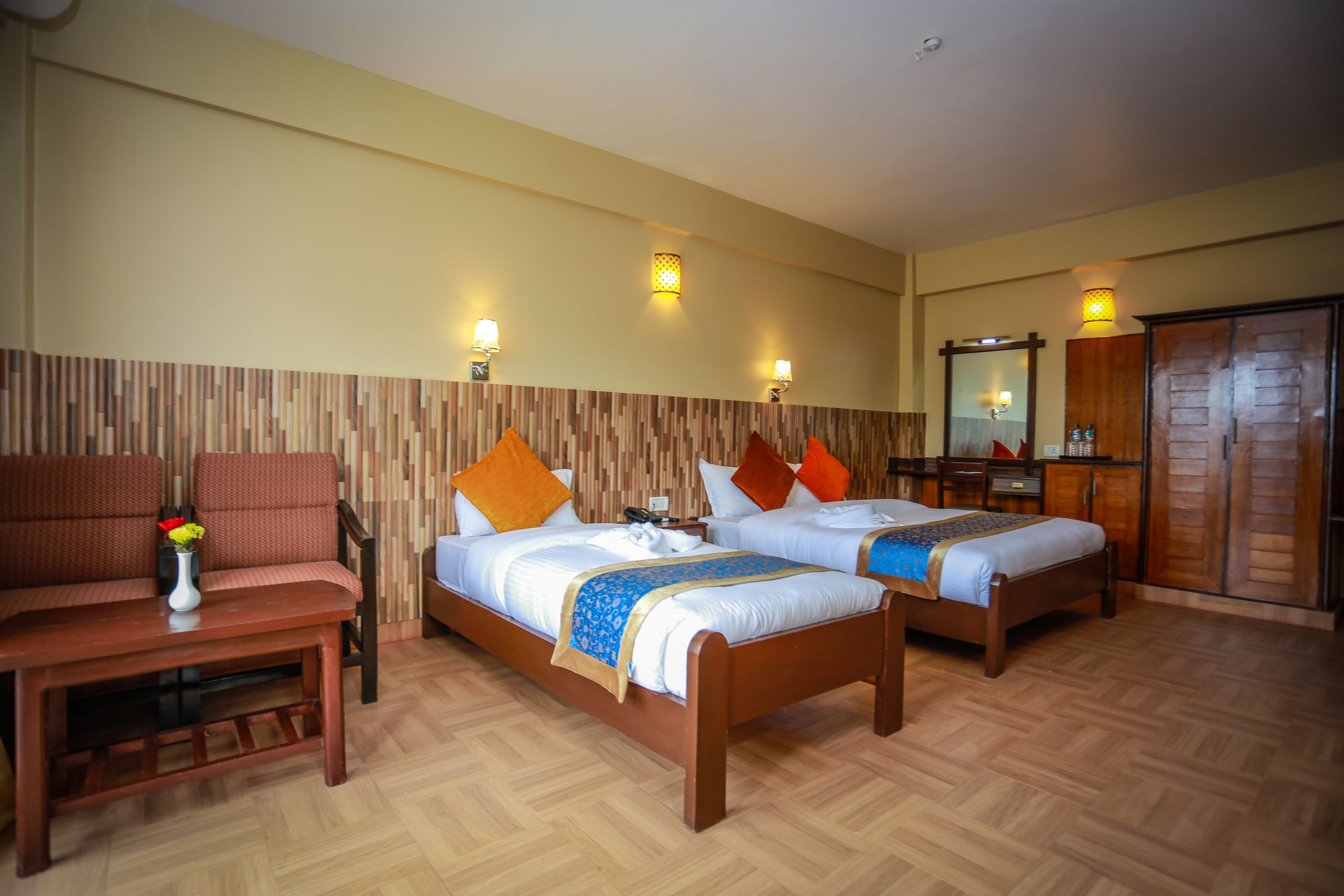 A hotel room with two beds, a wooden table, a sofa, and a mirror.