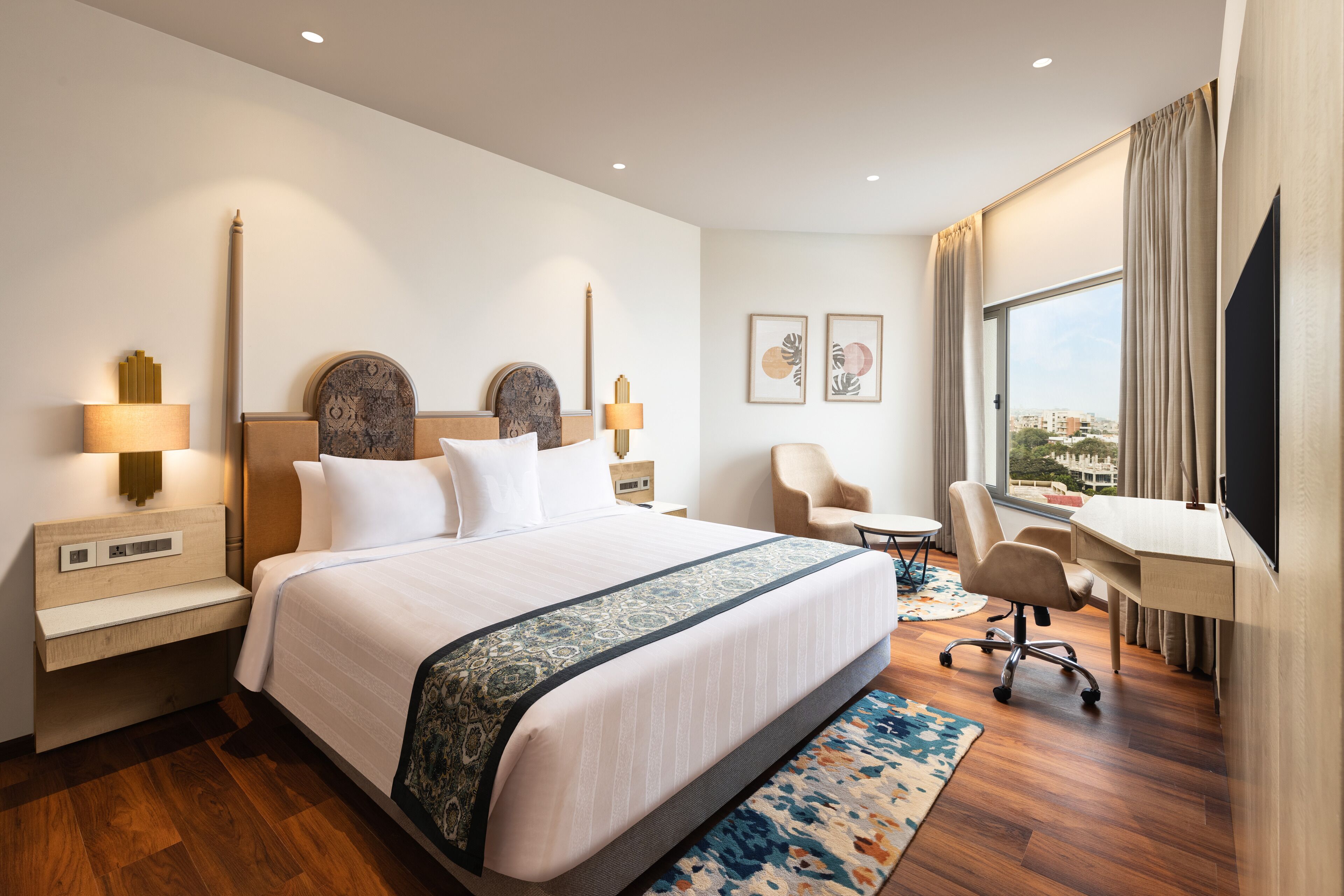 A hotel room with a large bed, a desk, a chair, and a TV.