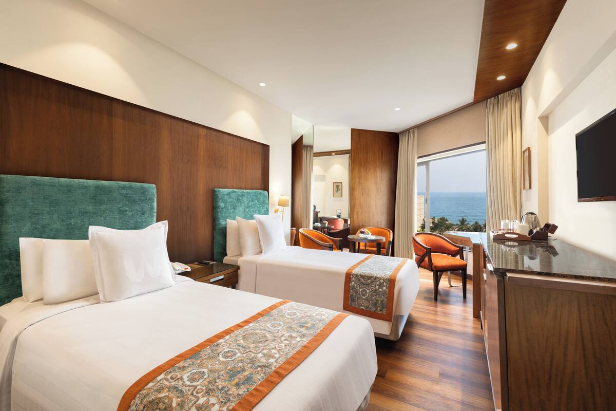 Habitación de hotel con dos camas, un escritorio, sillas, televisión y vista al océano.