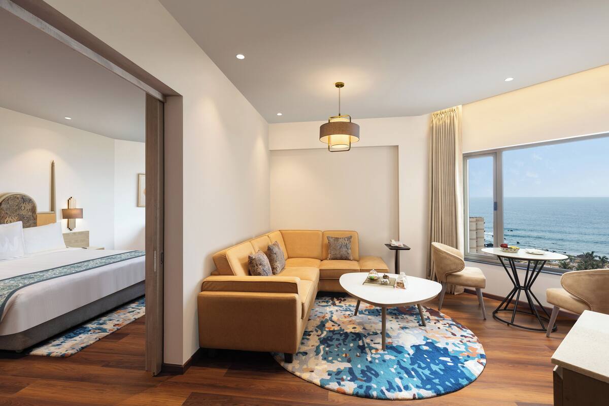 Habitación de hotel moderna con cama, sofá, mesa de centro y vista al océano.