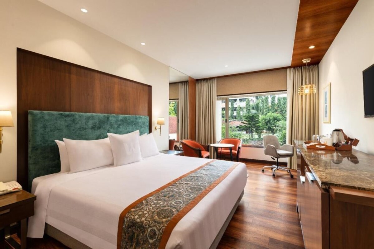 Habitación de hotel con una cama grande, un escritorio, una silla y vistas a zonas verdes.