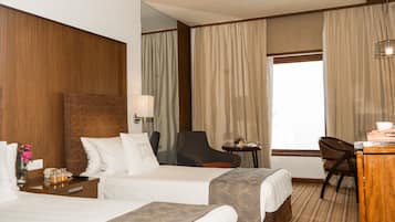 Una habitación de hotel con dos camas, un escritorio, una silla y un ventanal con cortinas.
