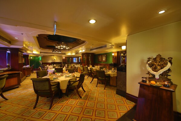 A restaurant with multiple tables and chairs, a patterned carpet, and a statue on a pedestal.