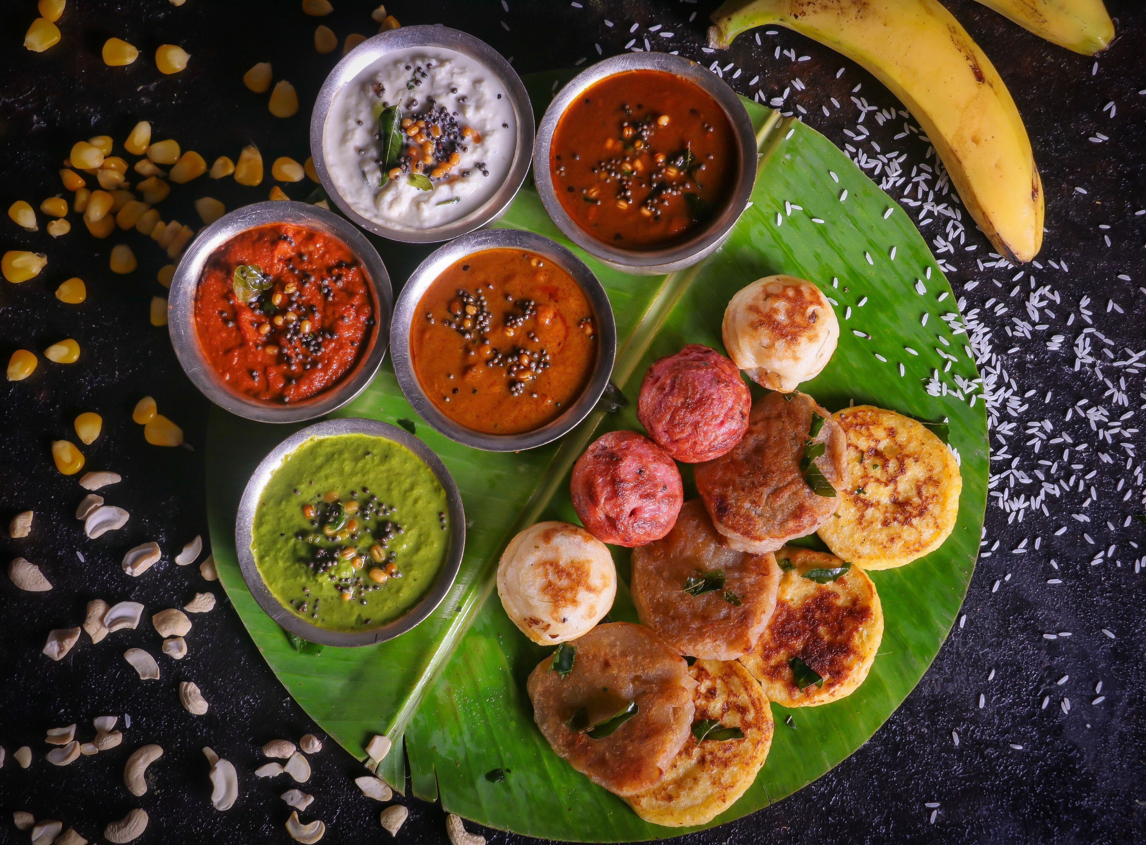 Verschiedene indische Gerichte, darunter Currys, Chutneys und Snacks, auf einem Bananenblatt.