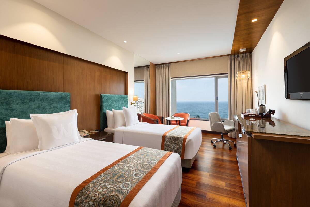 Habitación de hotel con dos camas, un escritorio, una silla, televisión y vista al océano.