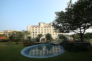 Un hotel con piscina, rodeado de vegetación y un gran árbol.