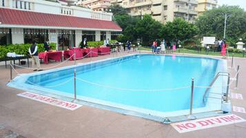 A swimming pool with a 'No Diving' sign, surrounded by tables and chairs, with a building in the background.