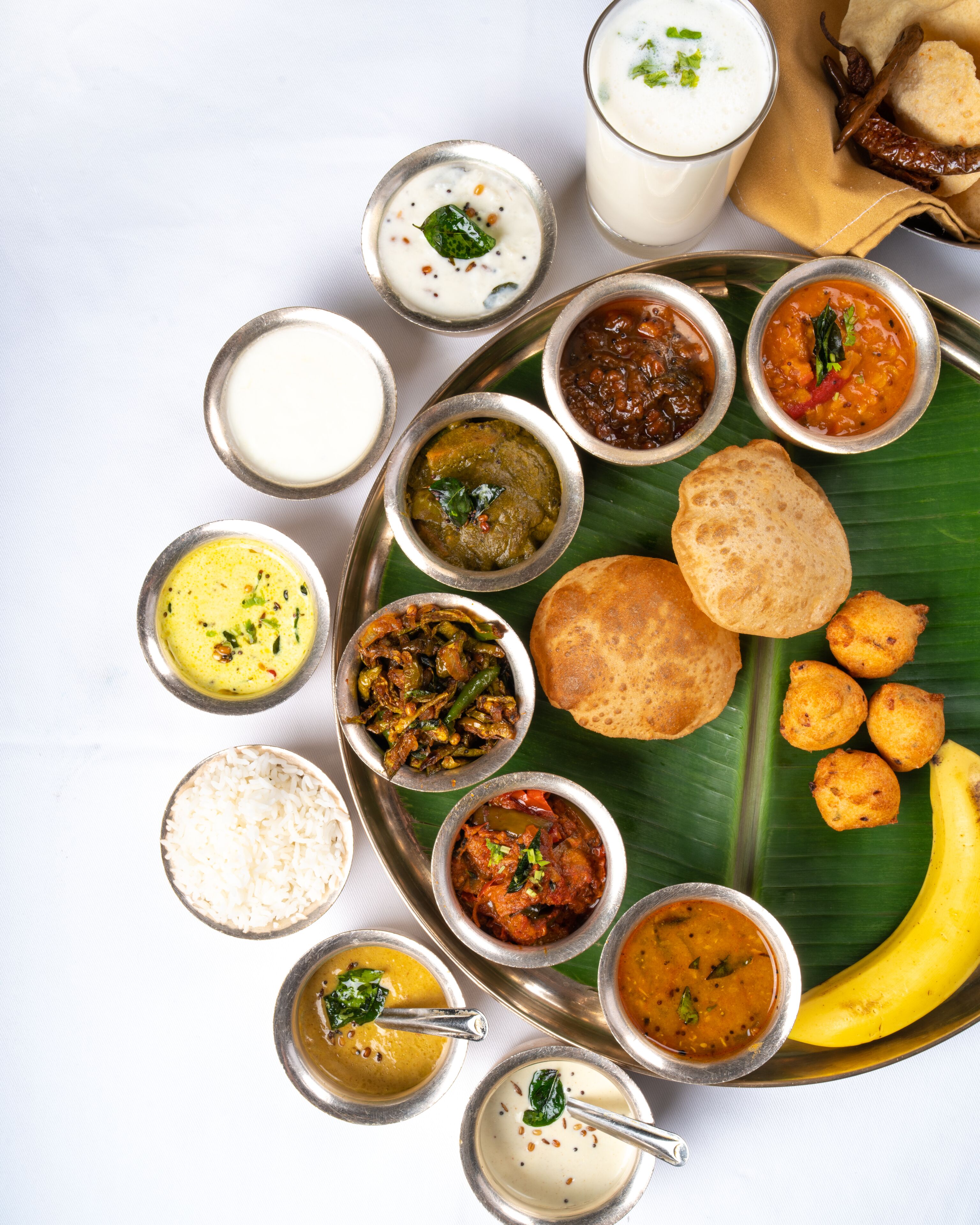 Diversos platos de la cocina india presentados sobre una hoja de plátano, con una bandeja de metal.