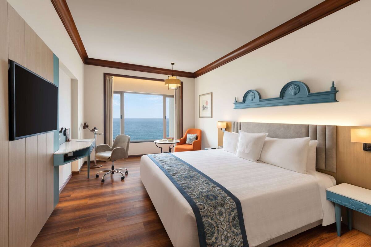 Habitación de hotel con una cama grande, un escritorio, una silla, una mesita y vistas al mar.