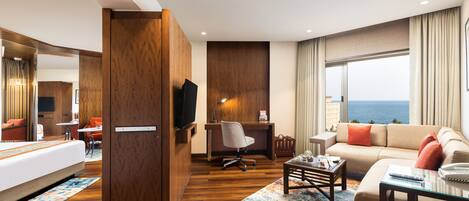A hotel room with a bed, a desk, a sofa, and a view of the ocean.