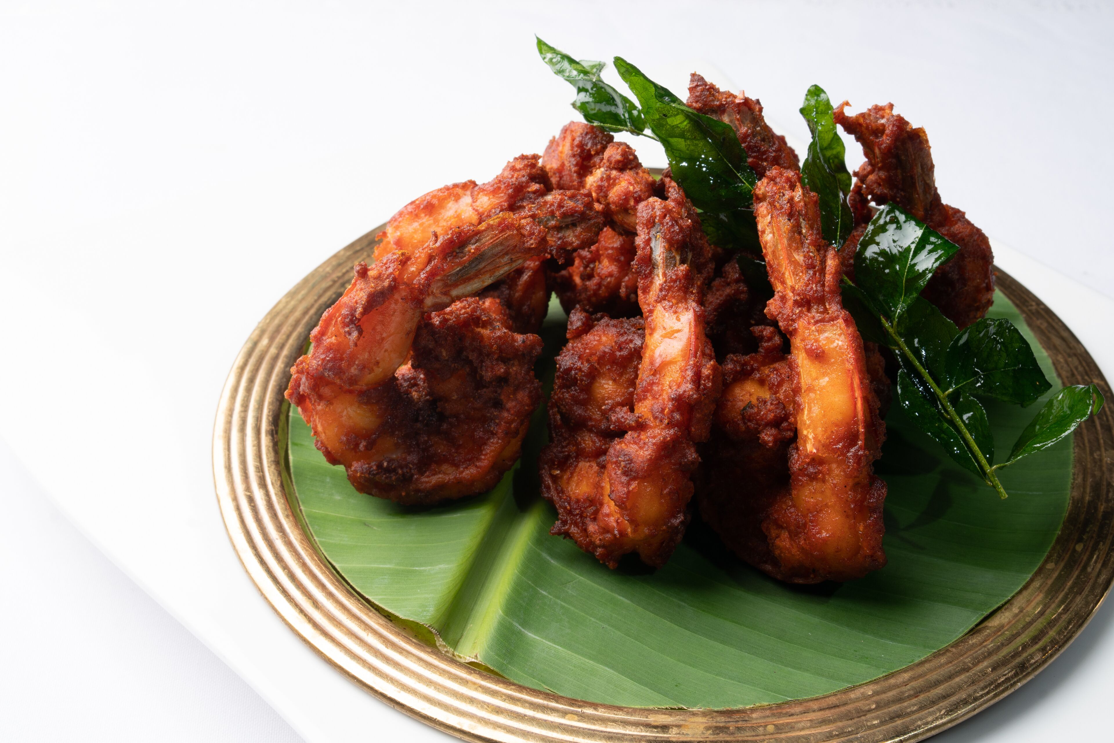 Un plato de pollo frito con una ramita de hoja verde sobre fondo blanco.