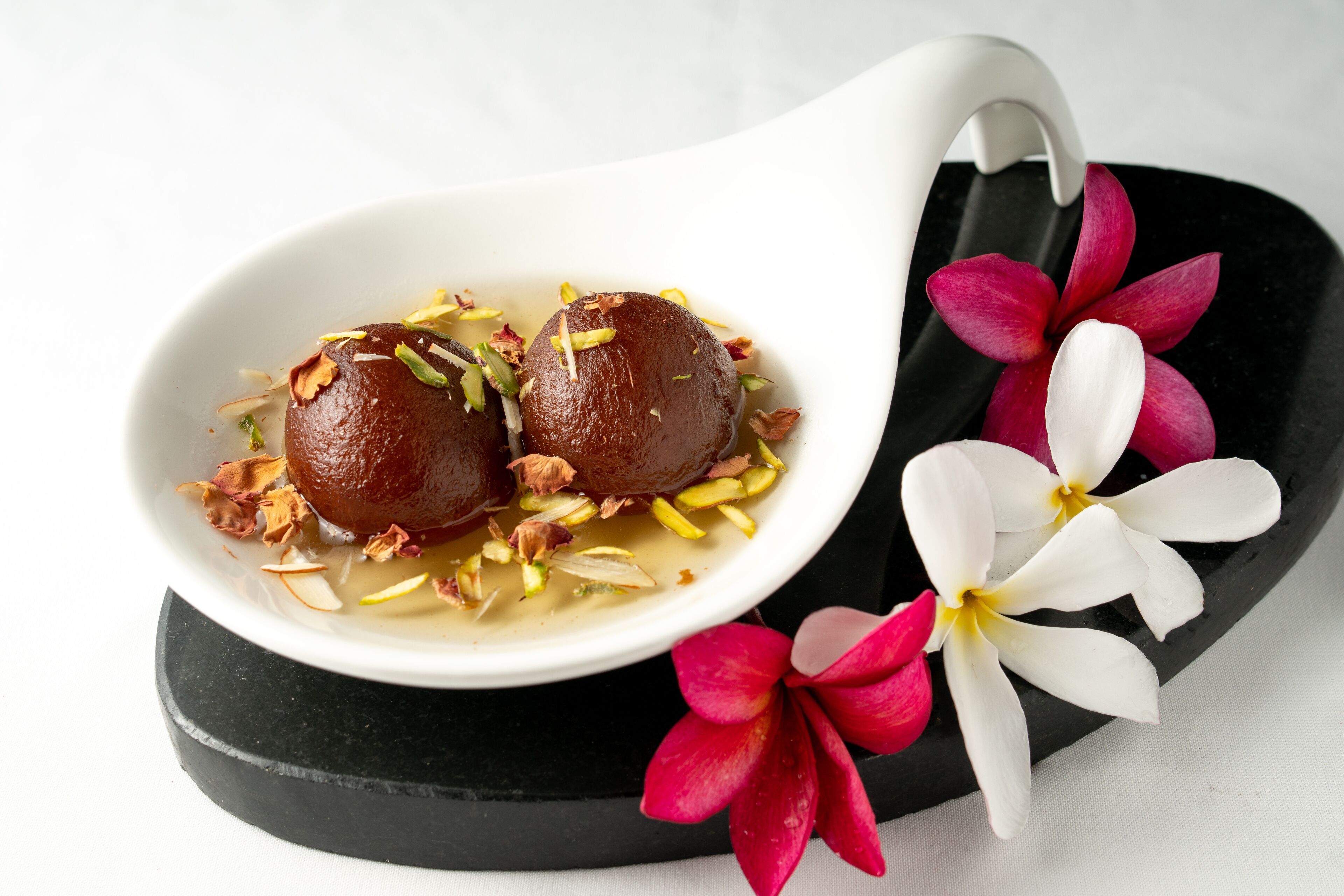 Un dessert composé de deux petites douceurs rondes, décorées de noix et de fleurs, et servi dans un bol blanc à la base noire.