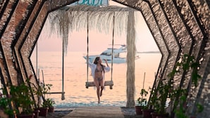 A person on a swing in a hexagonal structure with potted plants, overlooking a body of water with a boat in the background. - Litore Resort Hotel & Spa - All Inclusive (Alanya)