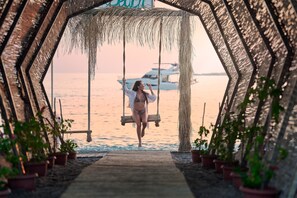 A person on a swing in a hexagonal structure with potted plants, overlooking a body of water with a boat in the background. - Litore Resort Hotel & Spa - All Inclusive (Alanya)