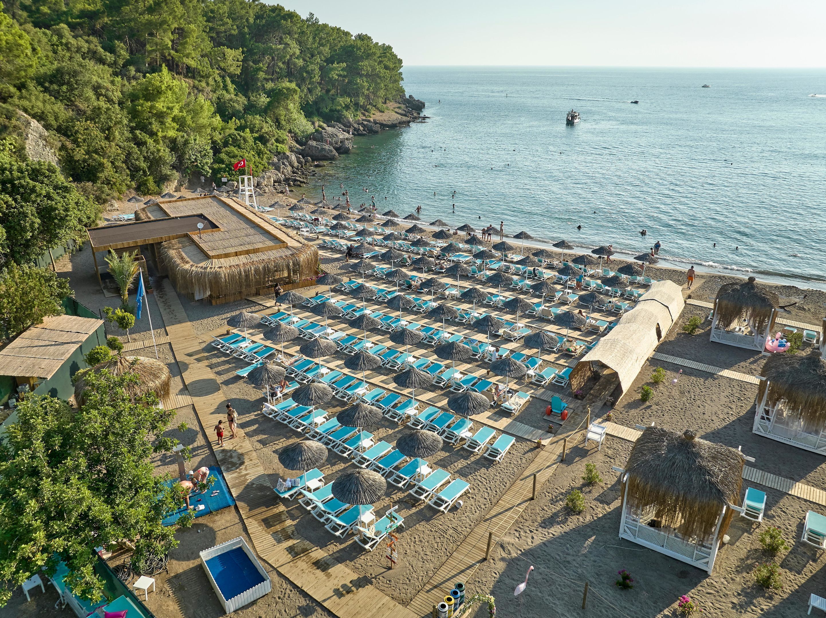 An aerial view of a beach resort with multiple sun loungers, a pool, and a thatched-roof building.
