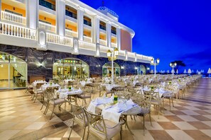 A hotel with outdoor dining tables, a checkered floor, and a large building with balconies.