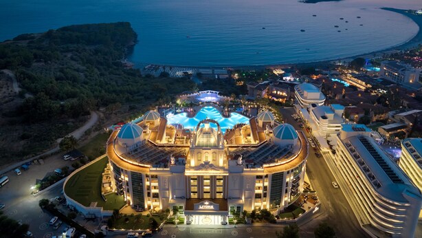 A large, circular hotel with a central pool, surrounded by a landscaped area and a body of water. - Litore Resort Hotel & Spa - All Inclusive (Alanya)