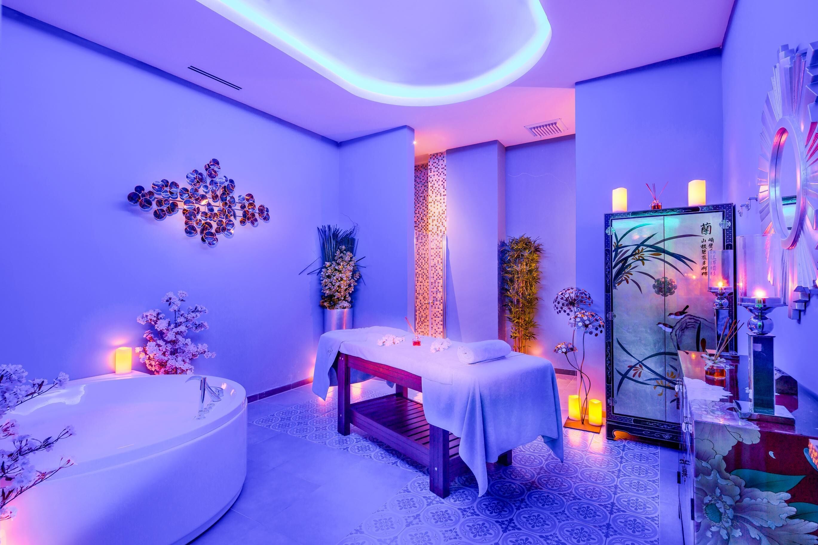 A spa room with a bathtub, a massage table, and decorative elements like flowers and candles.