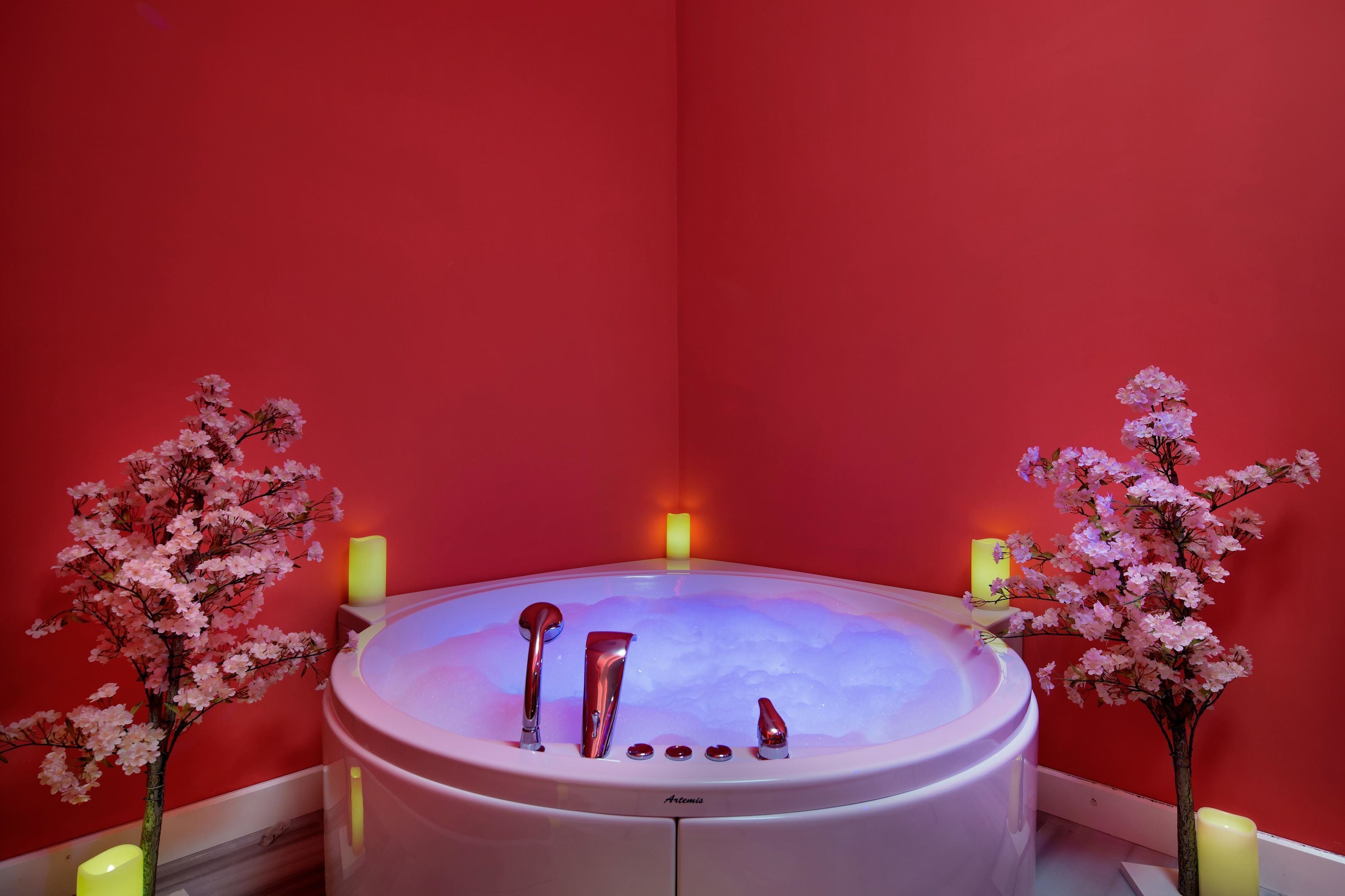 A spa room with a hot tub, two candles, and cherry blossom decorations.