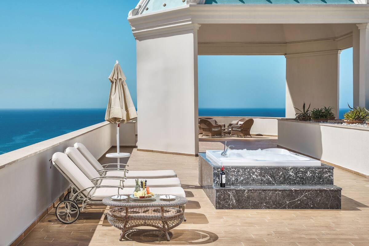 A rooftop terrace with lounge chairs, a hot tub, and a view of the ocean.