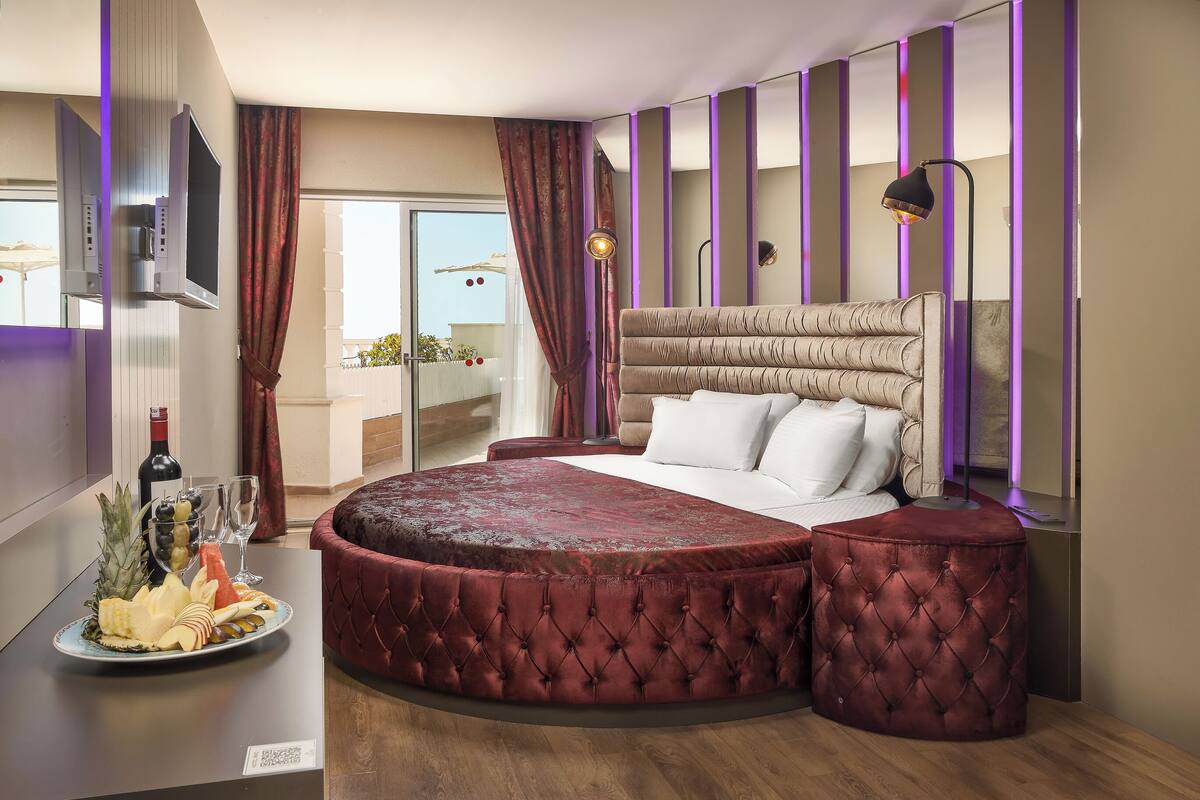 A modern bedroom with a round bed, a television, a minibar, and a balcony view.