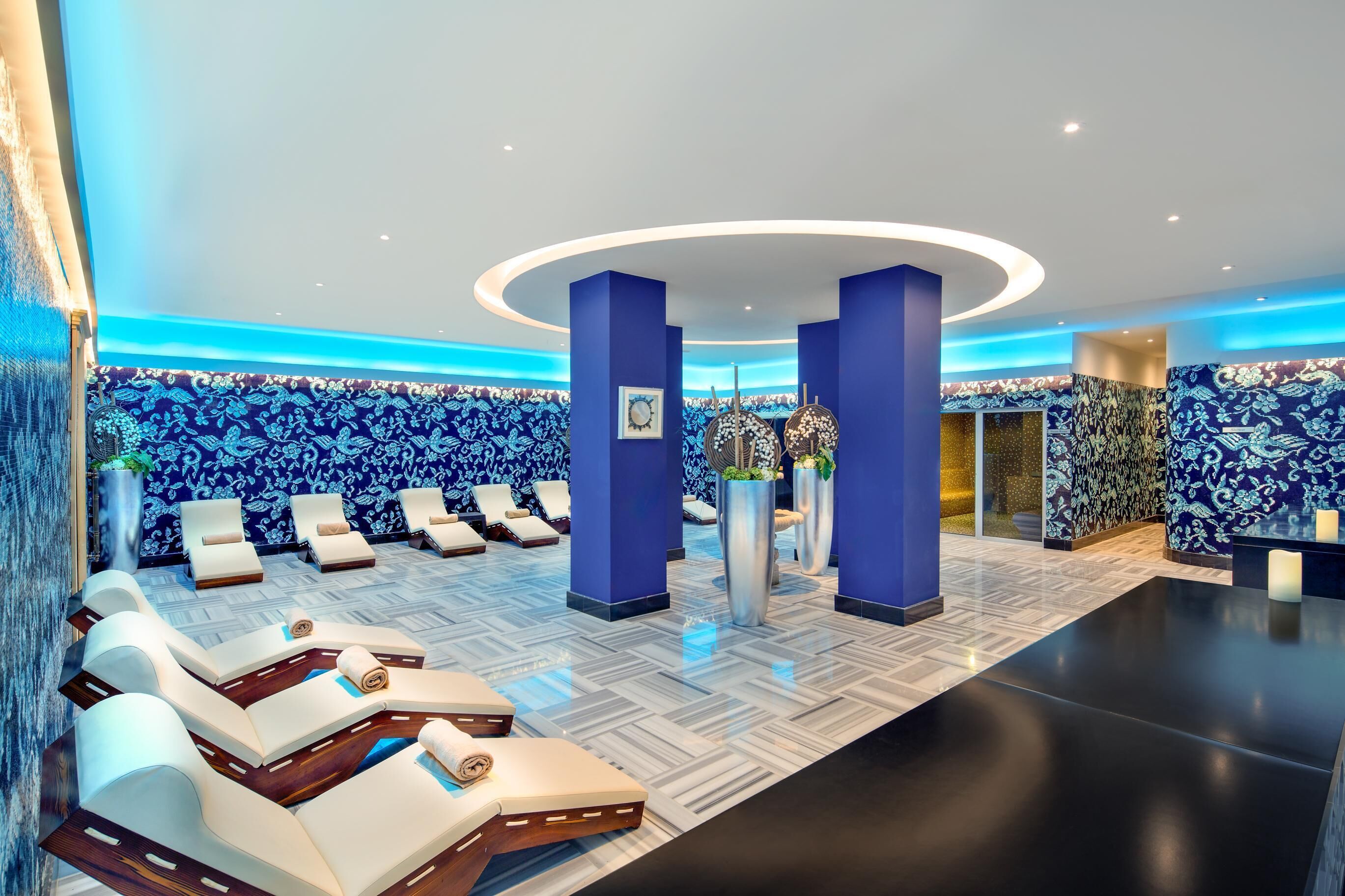Un hall de hotel con un muro de patrón azul y blanco, una recepción y varios sillones dispuestos en semicírculo.