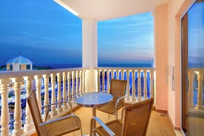 A balcony with a round table and wicker chairs, overlooking a coastal view.