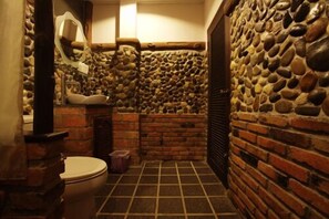 A bathroom with a stone wall, a tiled floor, and a toilet.