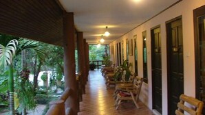 A covered corridor with wooden chairs and tables, surrounded by greenery. - Pathu Resort Ranong (Ranong)
