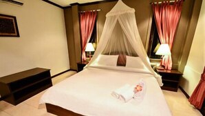 A hotel room with a four-poster bed, a bedside table with a lamp, and a bench at the foot of the bed. - Pathu Resort Ranong (Ranong)