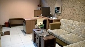 A living room with a sofa, a TV, a desk, and a small table. - Patria Palace Hotel (Blitar)