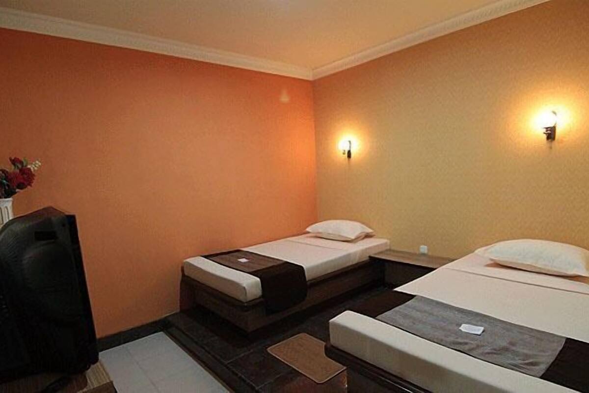 A hotel room with two single beds, a desk, and a chair.